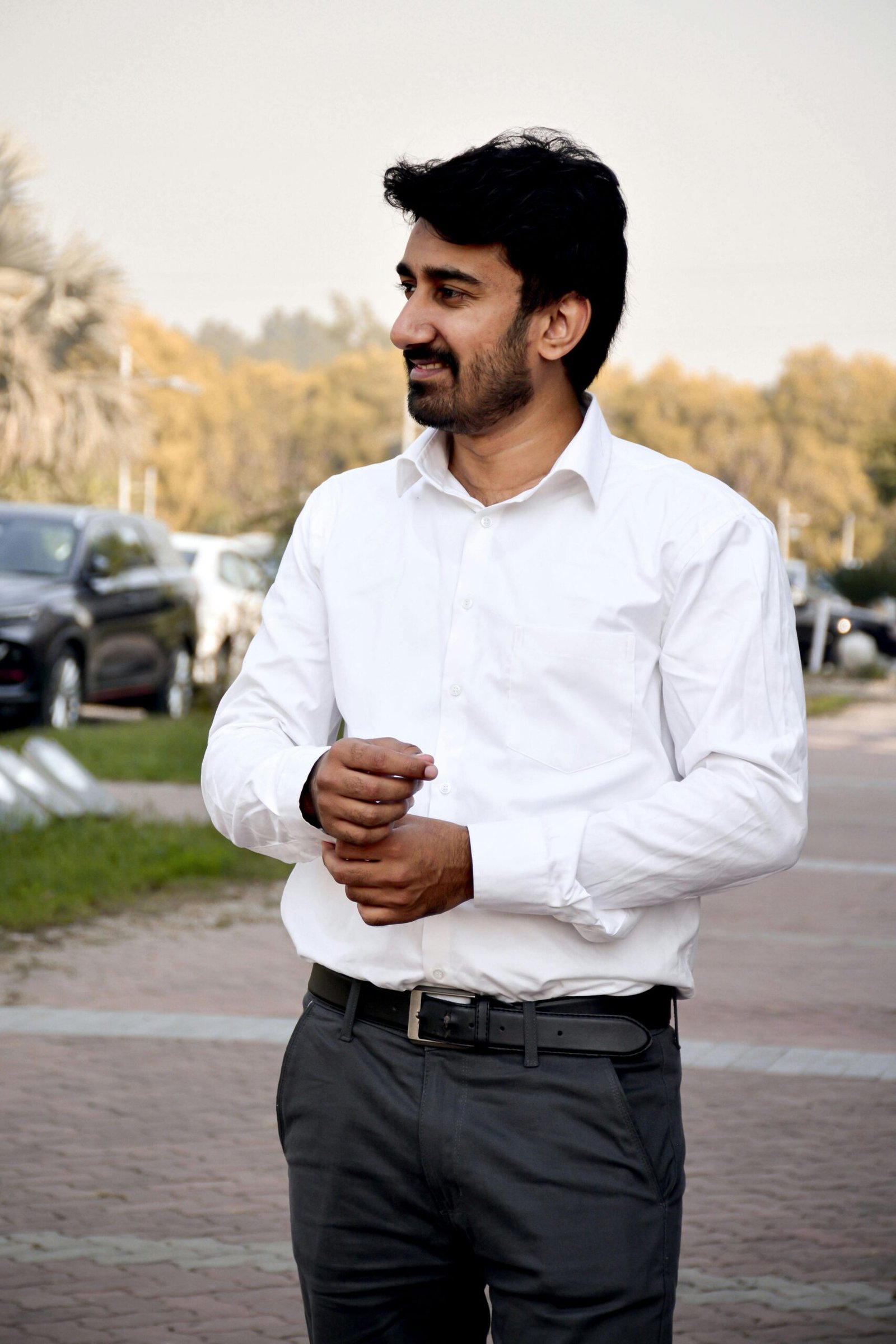 A man in a white shirt standing outdoors, exuding confidence.
